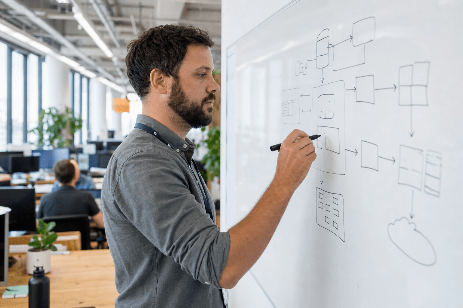 A male engineer in side profile sketches a governance flowchart on a whiteboard in a bright, open-plan Australian office, caught mid-stroke in a candid, unposed moment.