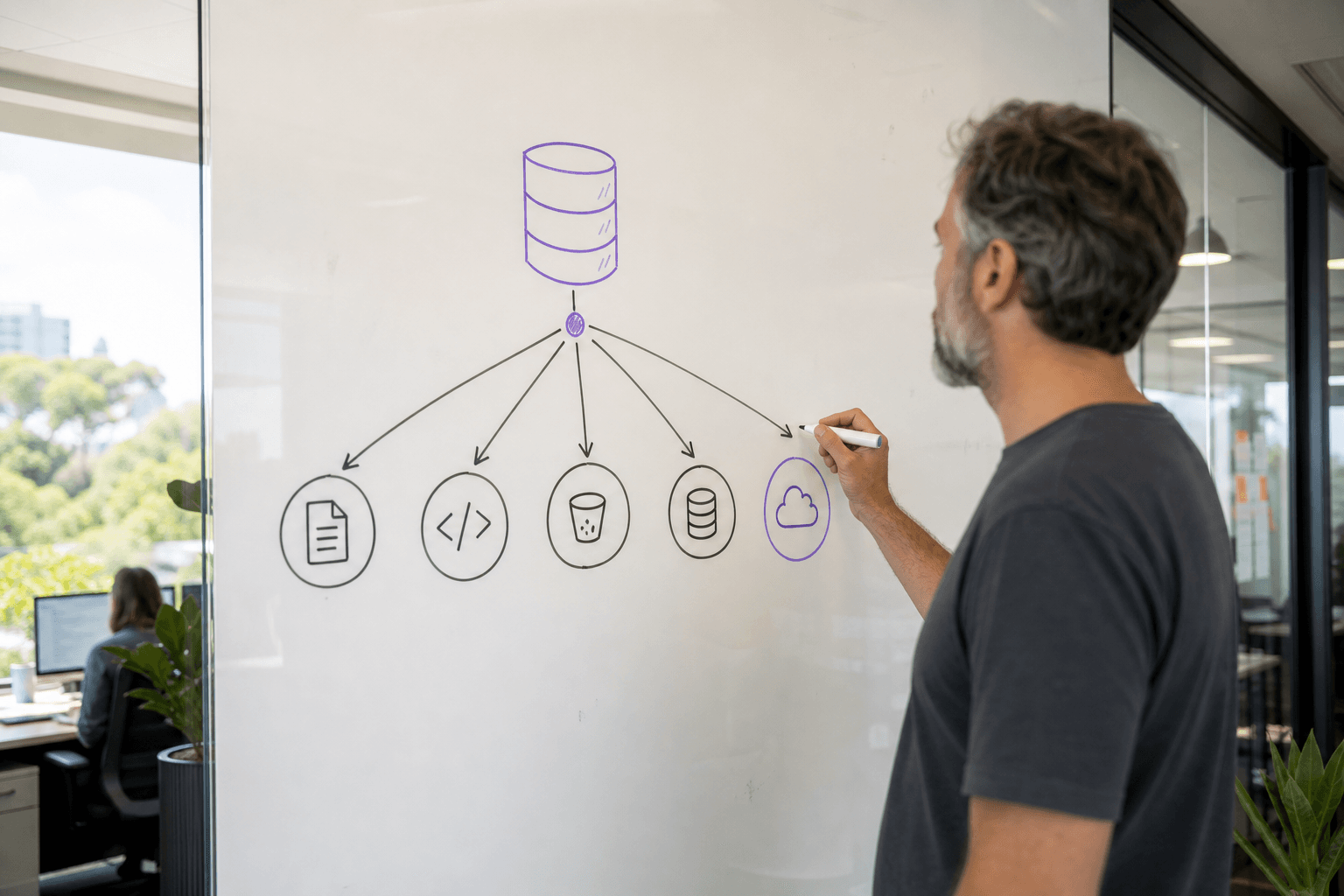 A male developer traces a hierarchical node-and-edge diagram on a whiteboard in a bright Australian open-plan office, illustrating how a central data warehouse connects to multiple structured source systems.